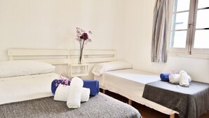 Habitación de hotel con dos camas individuales, una mesita de noche con un jarrón de flores y una ventana con cortinas a rayas.