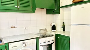 A kitchen with green cabinets, a white countertop, a Samsung washing machine, a gas stove, and a white refrigerator.