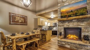 Un interior rústico con una mesa de comedor de madera, chimenea de piedra y zona de cocina.