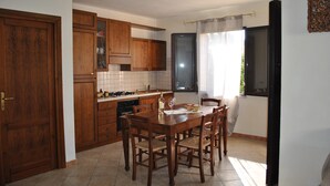 A kitchen with wooden cabinets, a dining table with chairs, a stove, and a window with curtains. - La Casa di Spinosella Agriturismo (Valledoria)