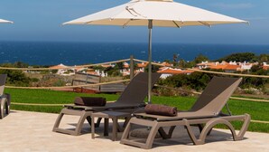 Two lounge chairs with a large umbrella, a rope barrier, and a view of the sea and houses in the background. - La Casa di Spinosella Agriturismo (Valledoria)