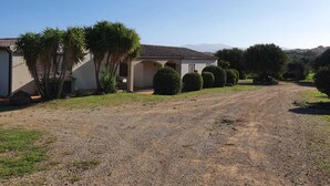 A single-story house with a gravel driveway, surrounded by well-maintained hedges and palm trees. - La Casa di Spinosella Agriturismo (Valledoria)
