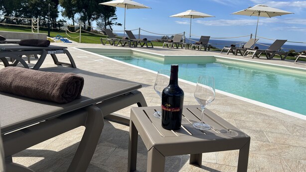 A poolside area with lounge chairs, umbrellas, and a bottle of wine on a table. - La Casa di Spinosella Agriturismo (Valledoria)