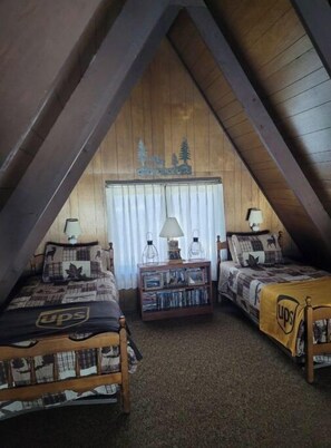 A cozy attic bedroom with two beds, a bookshelf, and a decorative wall.