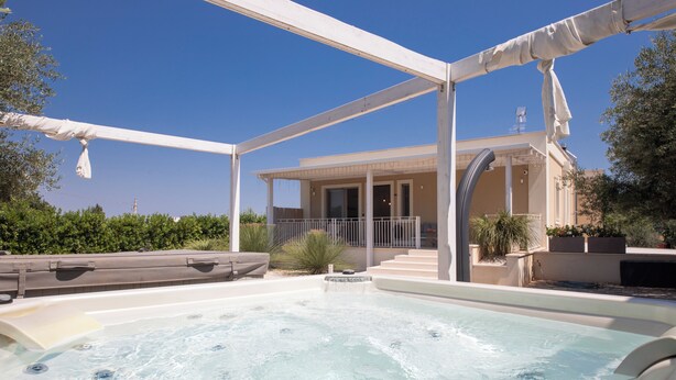 Een zone met een hottub, een overdekt terras, een zwembad en een gebouw op de achtergrond.