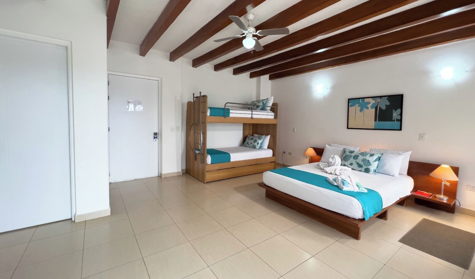 A bedroom with a large bed, a smaller bunk bed, a ceiling fan, and a painting on the wall.