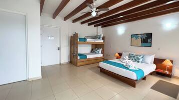 A bedroom with a large bed, a smaller bunk bed, a ceiling fan, and a painting on the wall.