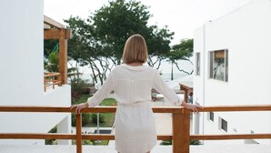 A person standing on a balcony with a view of a white building and a tree. - Hosteria del Parque Machalilla - Los Frailes (Machalilla)