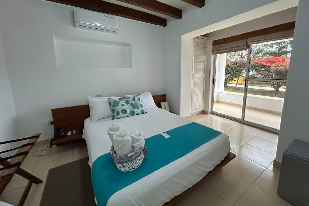 Quarto de hotel com cama, janela com vista, ventilador de teto e ar condicionado.