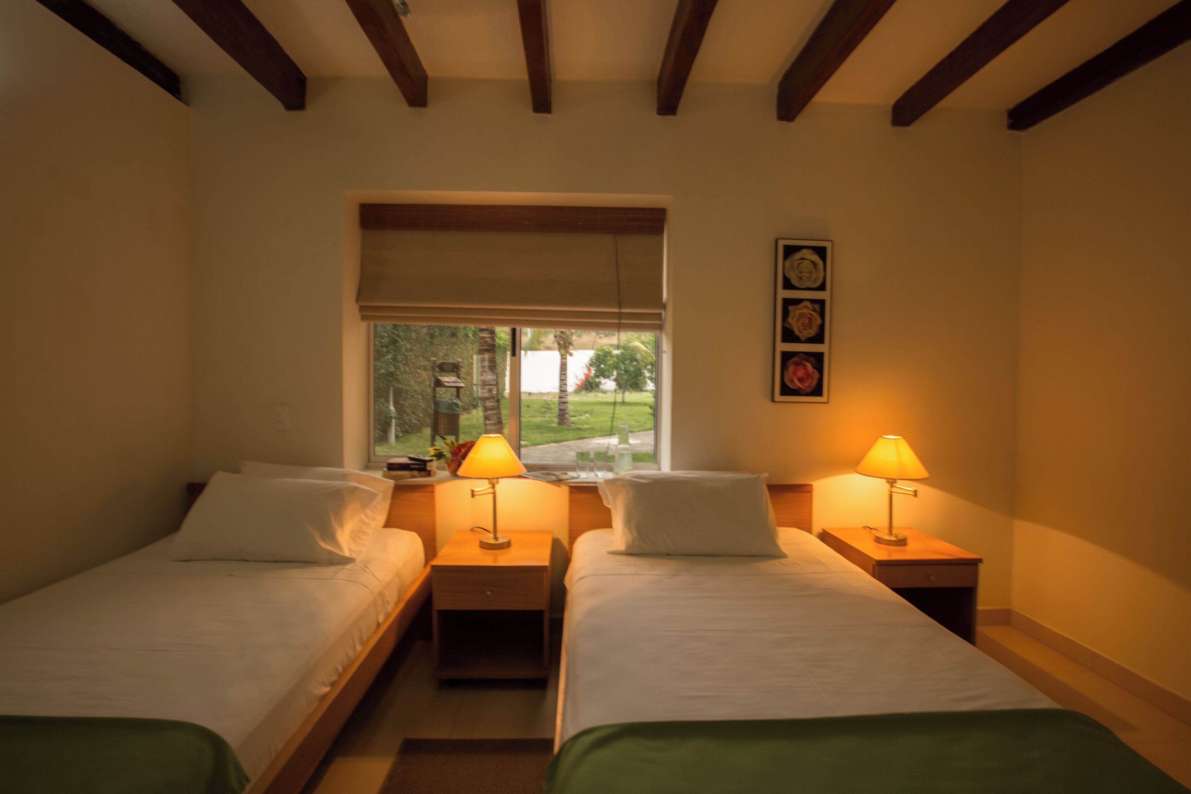 Een hotelkamer met twee eenpersoonsbedden, bedlampjes, een raam met uitzicht en een aan de muur hangend schilderij.