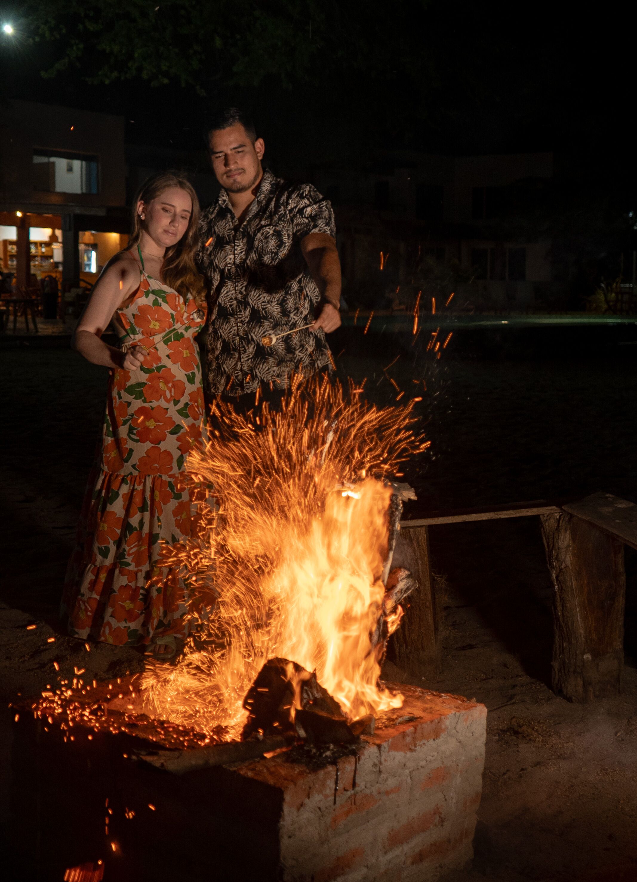 A couple standing by a fire pit at night.