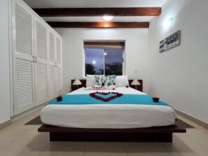 A bedroom with a bed, a window, a night sky view, a wall clock, and a door with louvered shutters. - Hosteria del Parque Machalilla - Los Frailes (Machalilla)