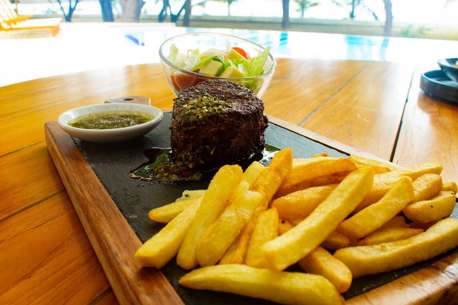 Un plato de carne con papas fritas y ensalada sobre una mesa de madera.