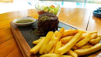 Un plato de carne con papas fritas y ensalada sobre una mesa de madera.