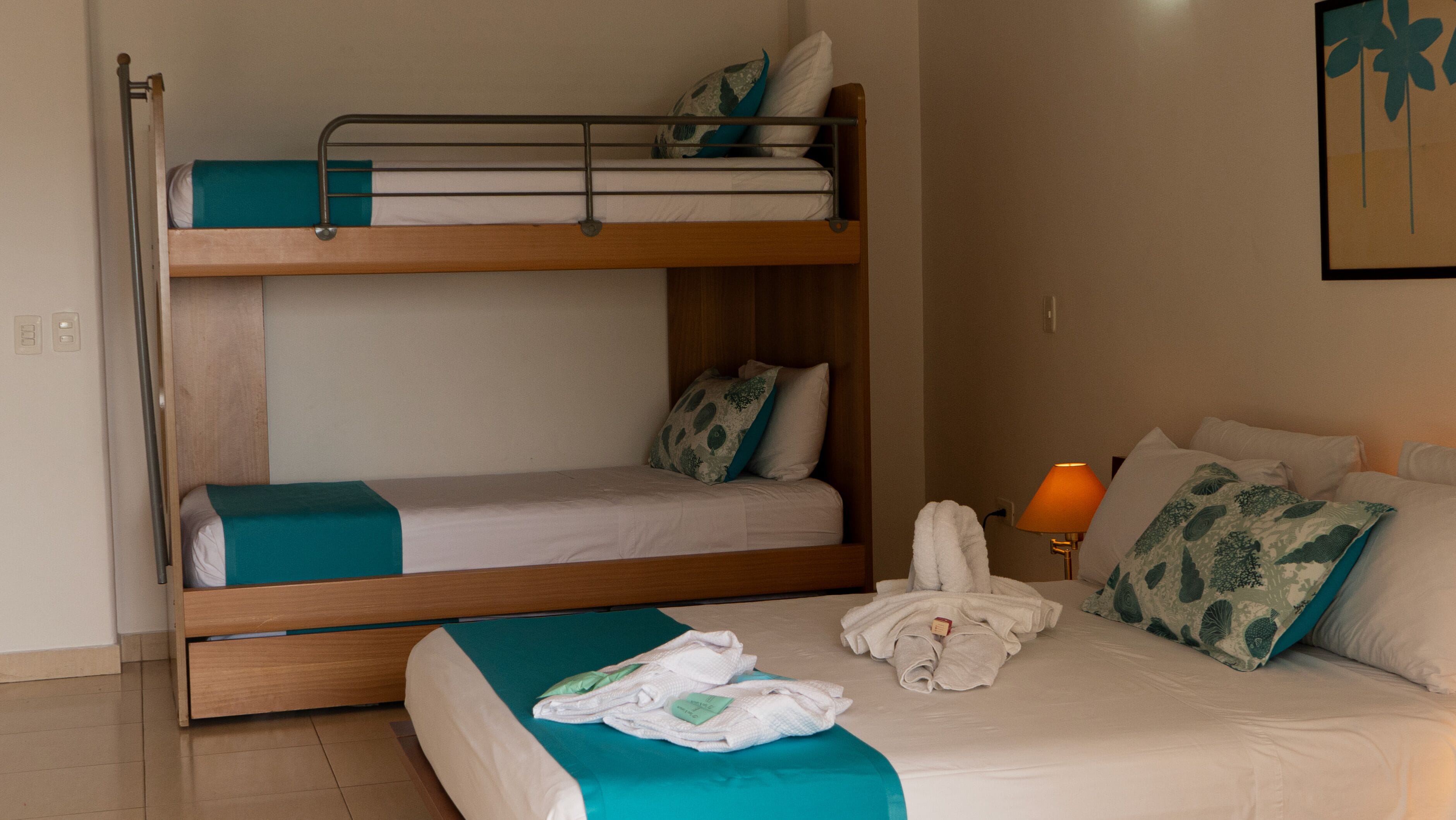 Una camera d'albergo con un letto a castello, un letto singolo e un comodino con una lampada.