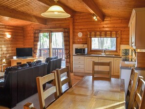 A cozy cabin interior with a living area featuring a sofa and chairs, a dining table, a kitchen with a microwave, and a large window with a view of trees. - 3 bedroom accommodation in Kenwick, near Louth (Kenwick, near Louth)
