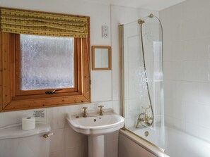 Ein Badezimmer mit Holzfenster, Waschbecken in Weiß und einer Duschkabine aus Glas.