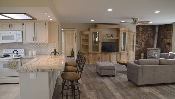 A spacious kitchen with a large island, bar stools, and a dining area with a stone accent wall. -  Newly remodeled 3 bedroom home located near Yosemite and bass lake (Oakhurst)