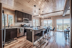 Une cuisine moderne avec un plancher en bois, des meubles de couleur sombre et un îlot central doté de tabourets de bar.