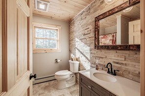 Une salle de bain avec un plafond en bois, une fenêtre, des toilettes, un lavabo et un miroir.