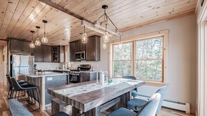 Una cocina moderna con vigas de madera en el techo, iluminación colgante y una isla grande con taburetes de bar.