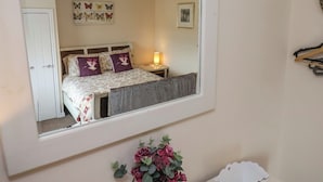 A bedroom with a bed, a bedside table, a lamp, a mirror, and a door. - North Terrace (Saltburn-by-the-Sea)