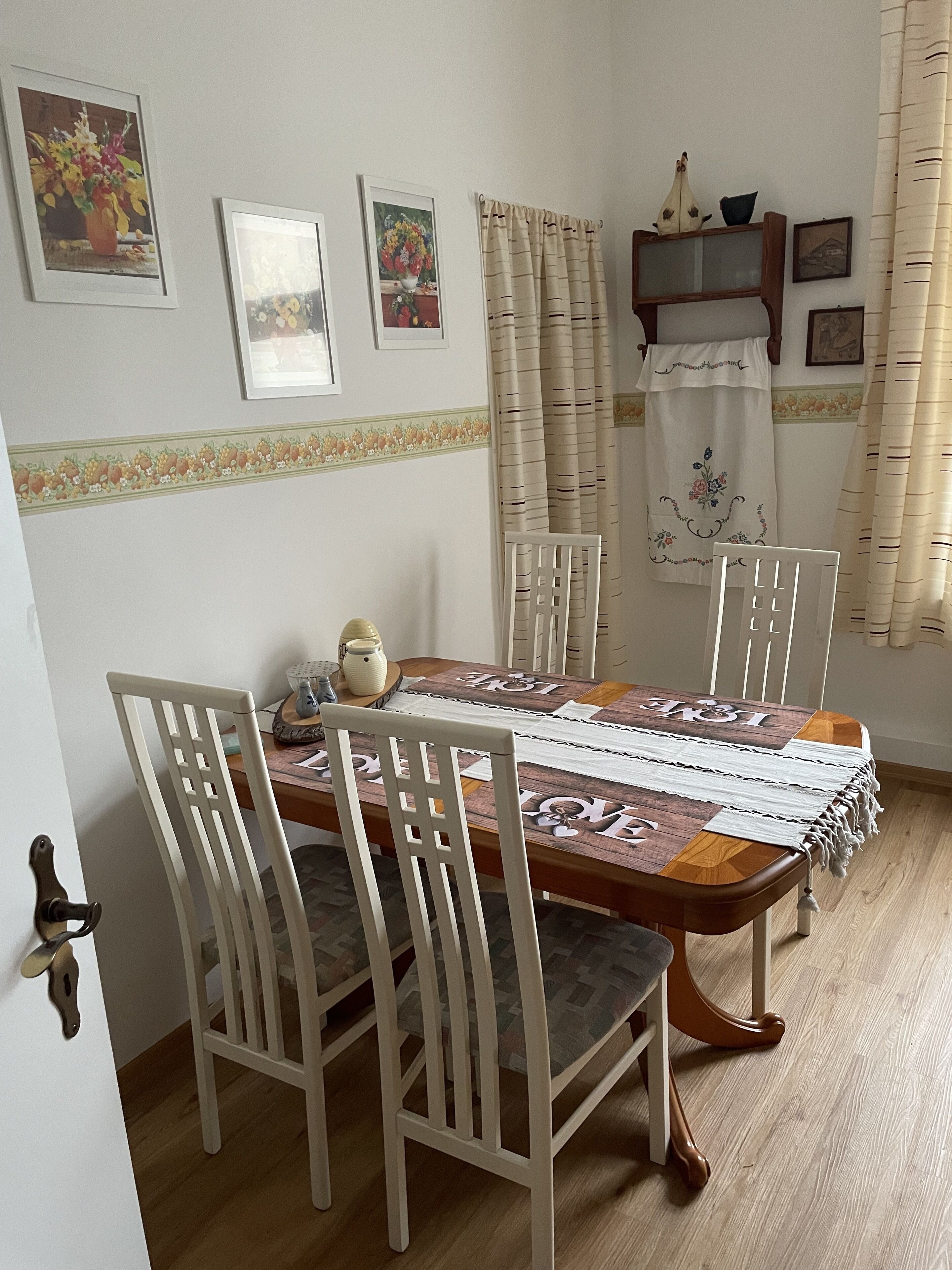 A dining area with a wooden table, white chairs, and a floral border on the wall.