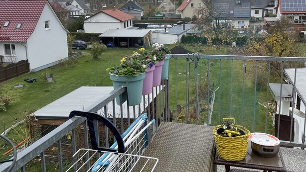 A balcony with a wicker table, a chair, and potted plants. - Colorful city on the Elde 2 (Grabow)