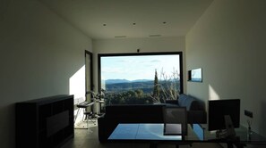 Un salon moderne avec une grande fenêtre, un canapé, une table basse et un téléviseur à écran plat.
