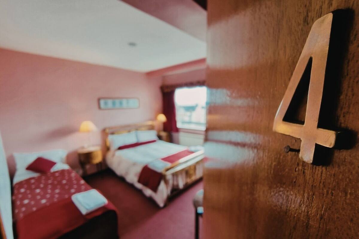 A room with two beds, a wooden door with a number, and a window.