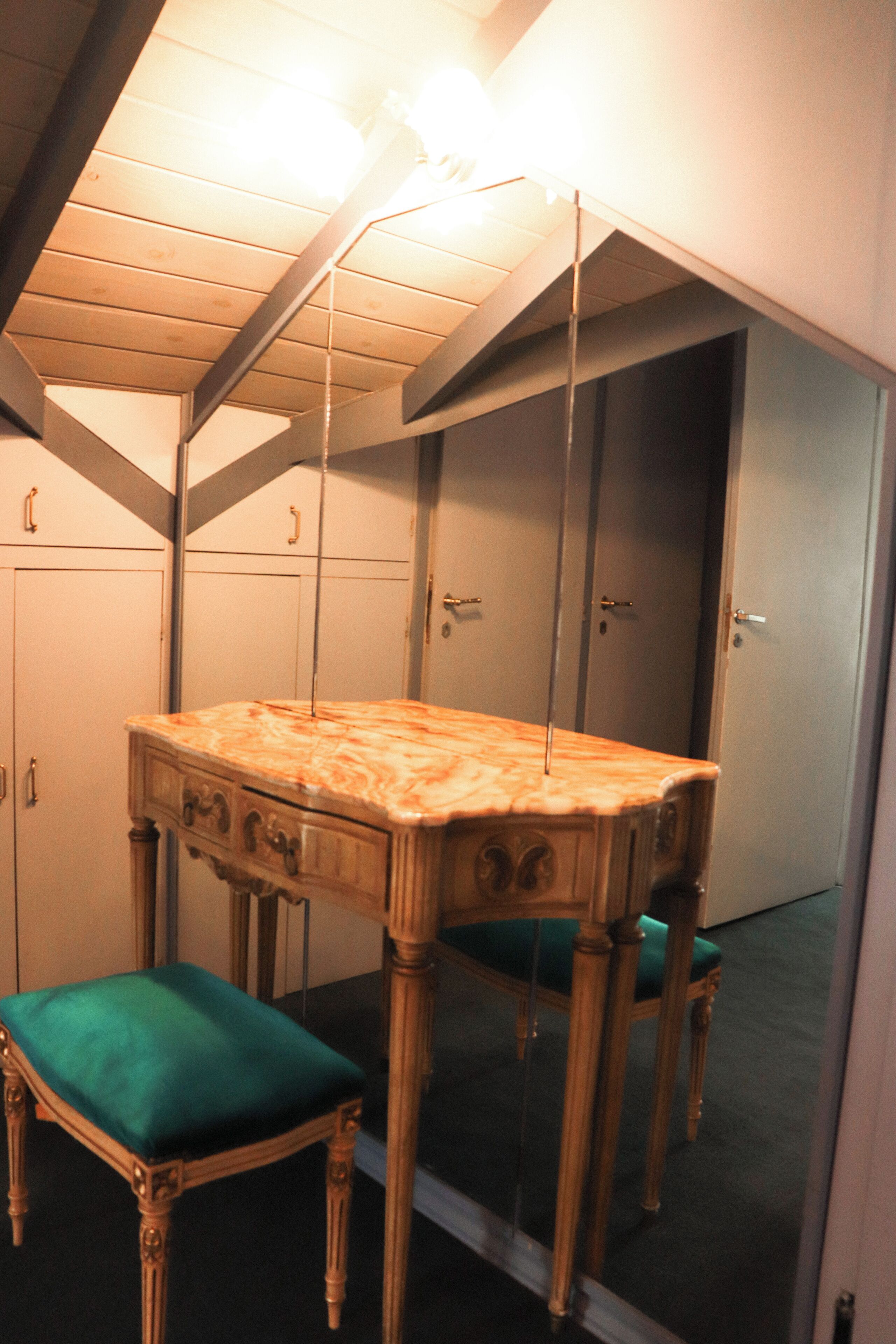 Quarto com mesa de toucador de madeira, cadeira estofada verde e espelho sobre a mesa.