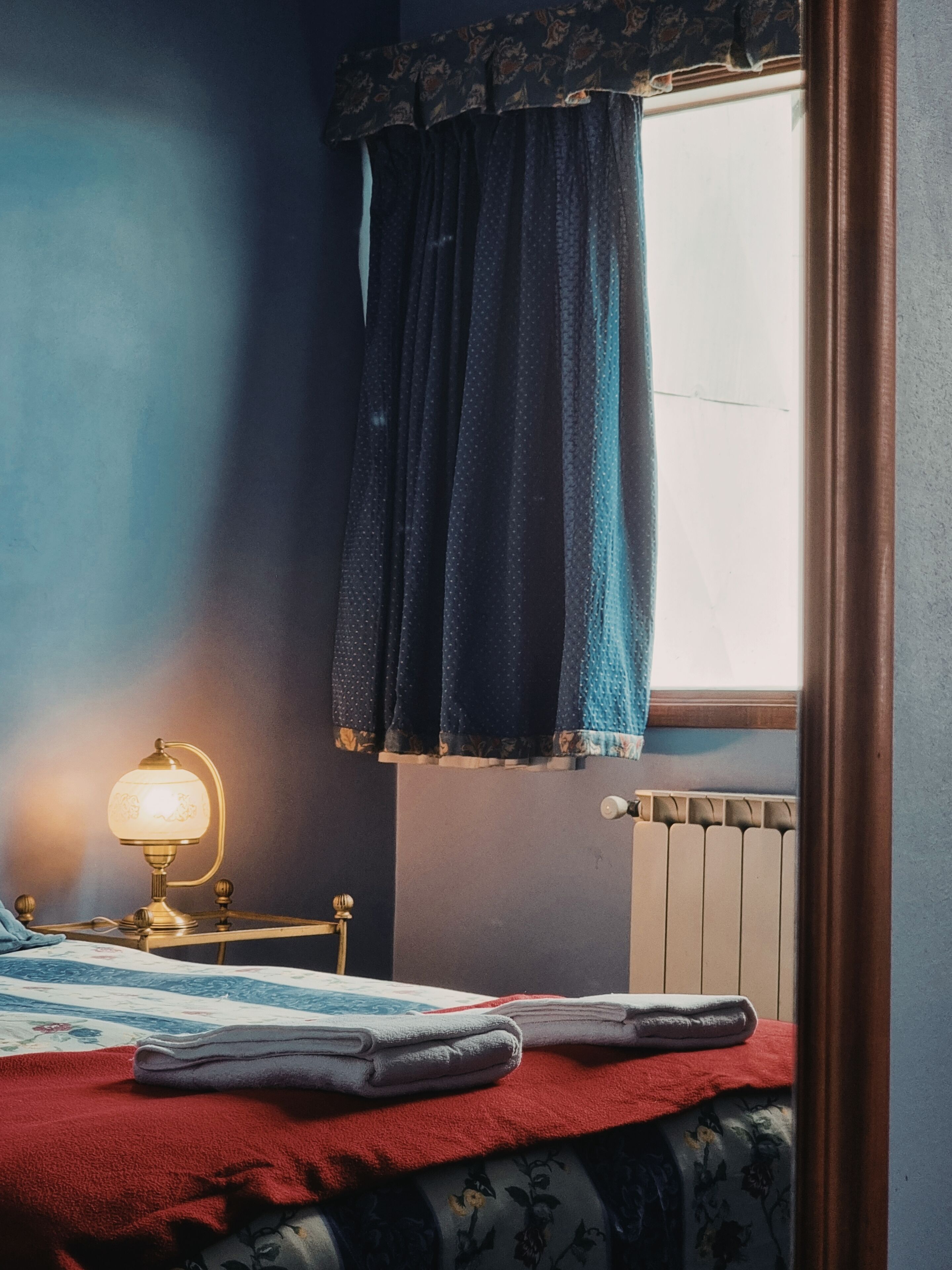 Ein Schlafzimmer mit einem Bett, einem Nachttisch, einer Lampe und einem Fenster mit Vorhängen.