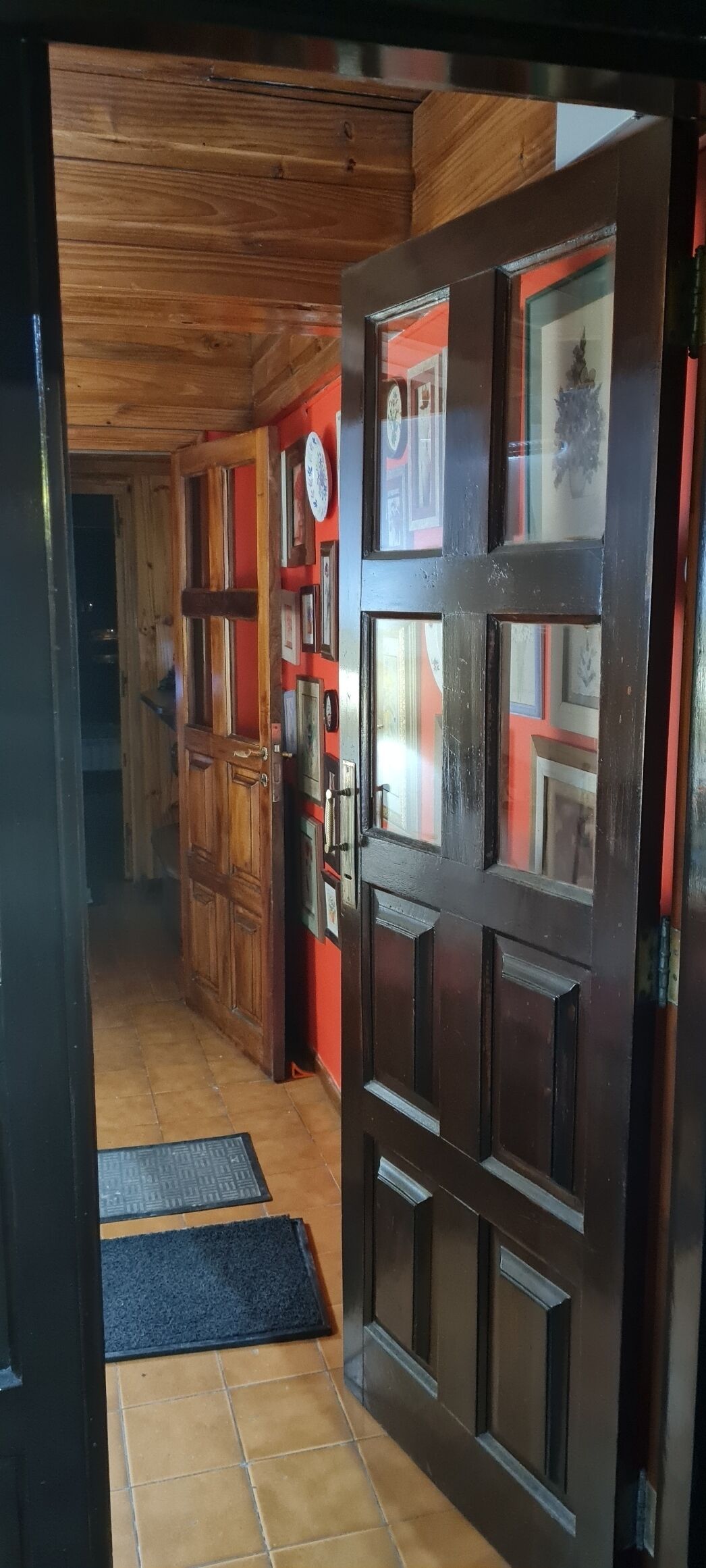 Un corridoio con porte in legno, un orologio e una parete rossa con quadri appesi.
