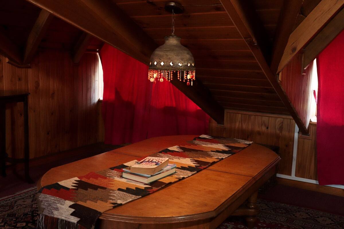 A cozy room with a wooden table, a hanging light fixture, and a red curtain.