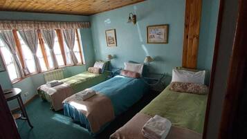 Una habitación con dos camas individuales, una mesita y un ventanal con cortinas.