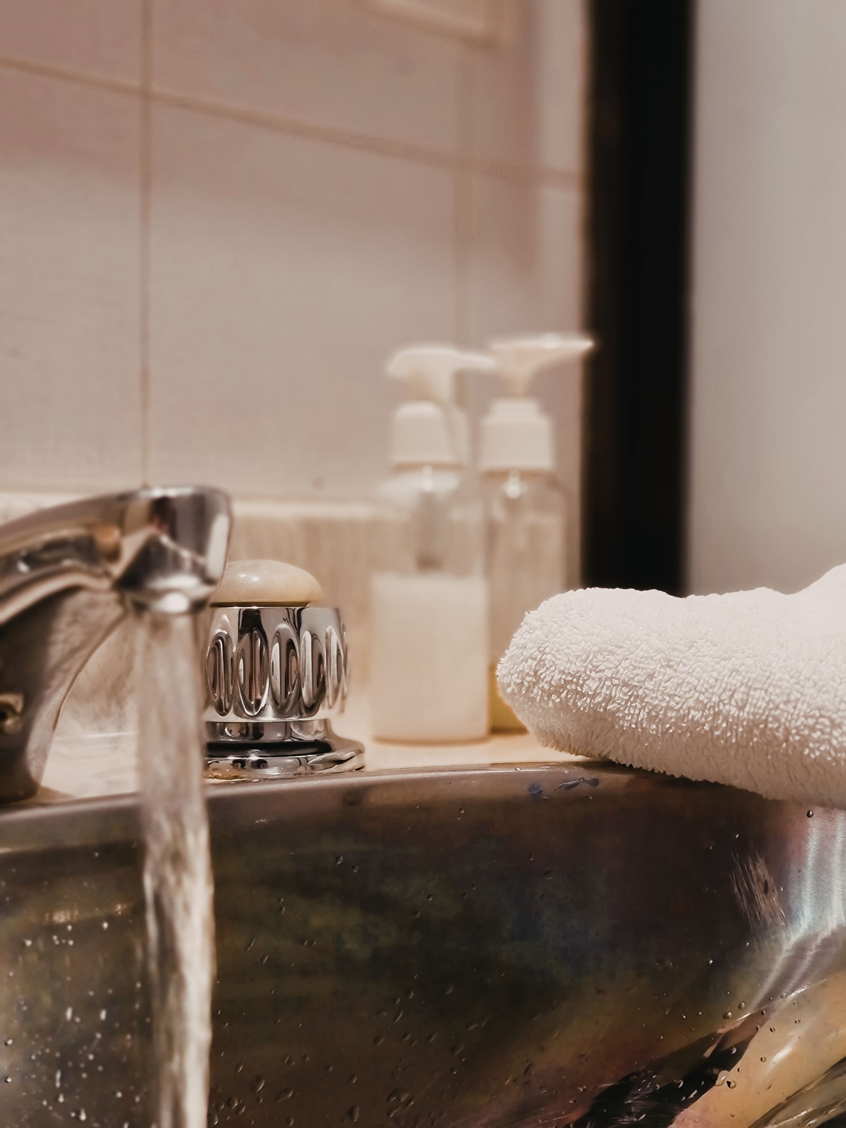 A bathroom sink with running water, soap dispensers, and a white towel.