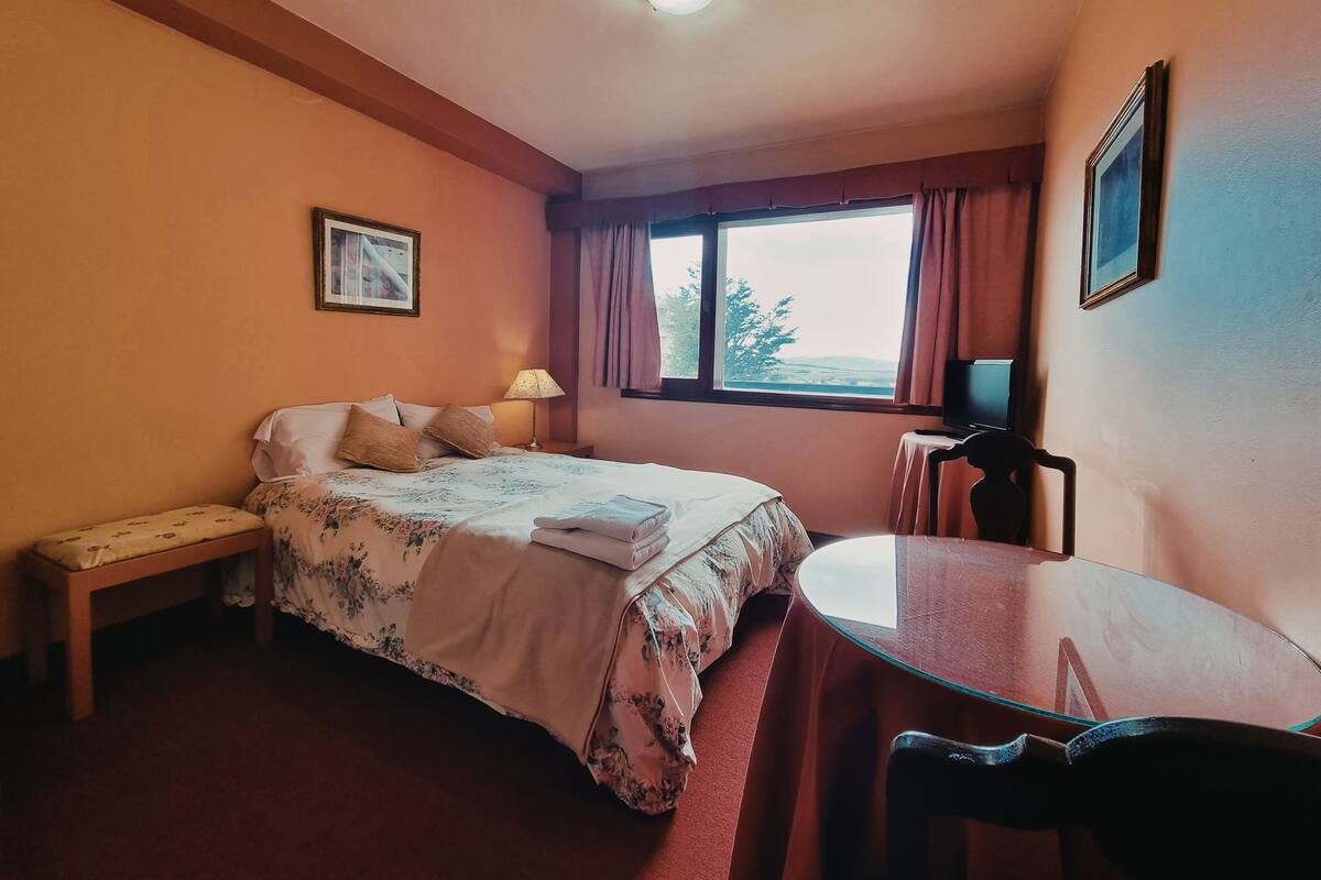 A hotel room with a bed, a bedside table, a chair, a desk, and a window with curtains.