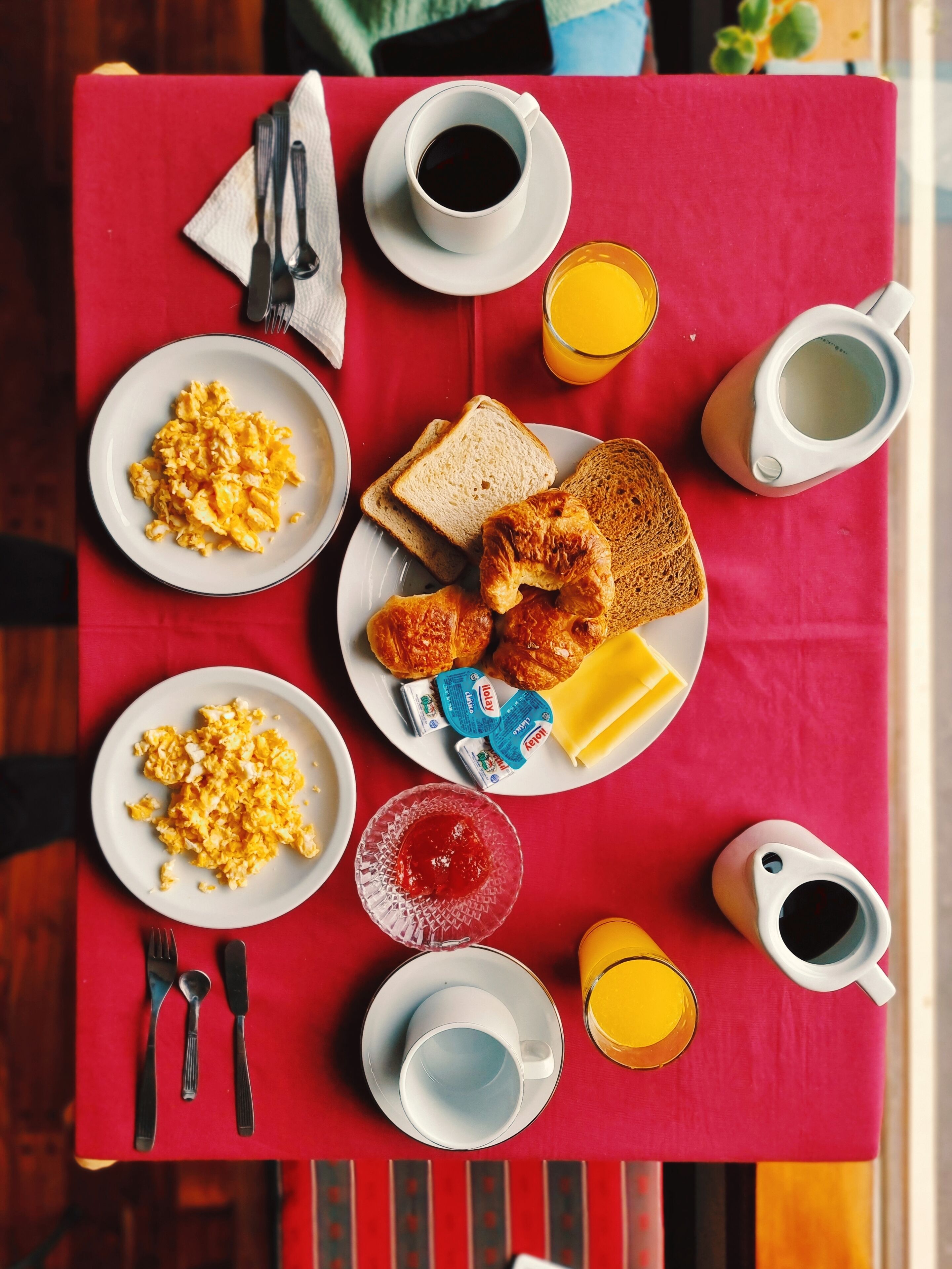 Ett frukostbord med äggröra, rostmackor, croissanter, smör, sylt, kaffe och apelsinjuice.