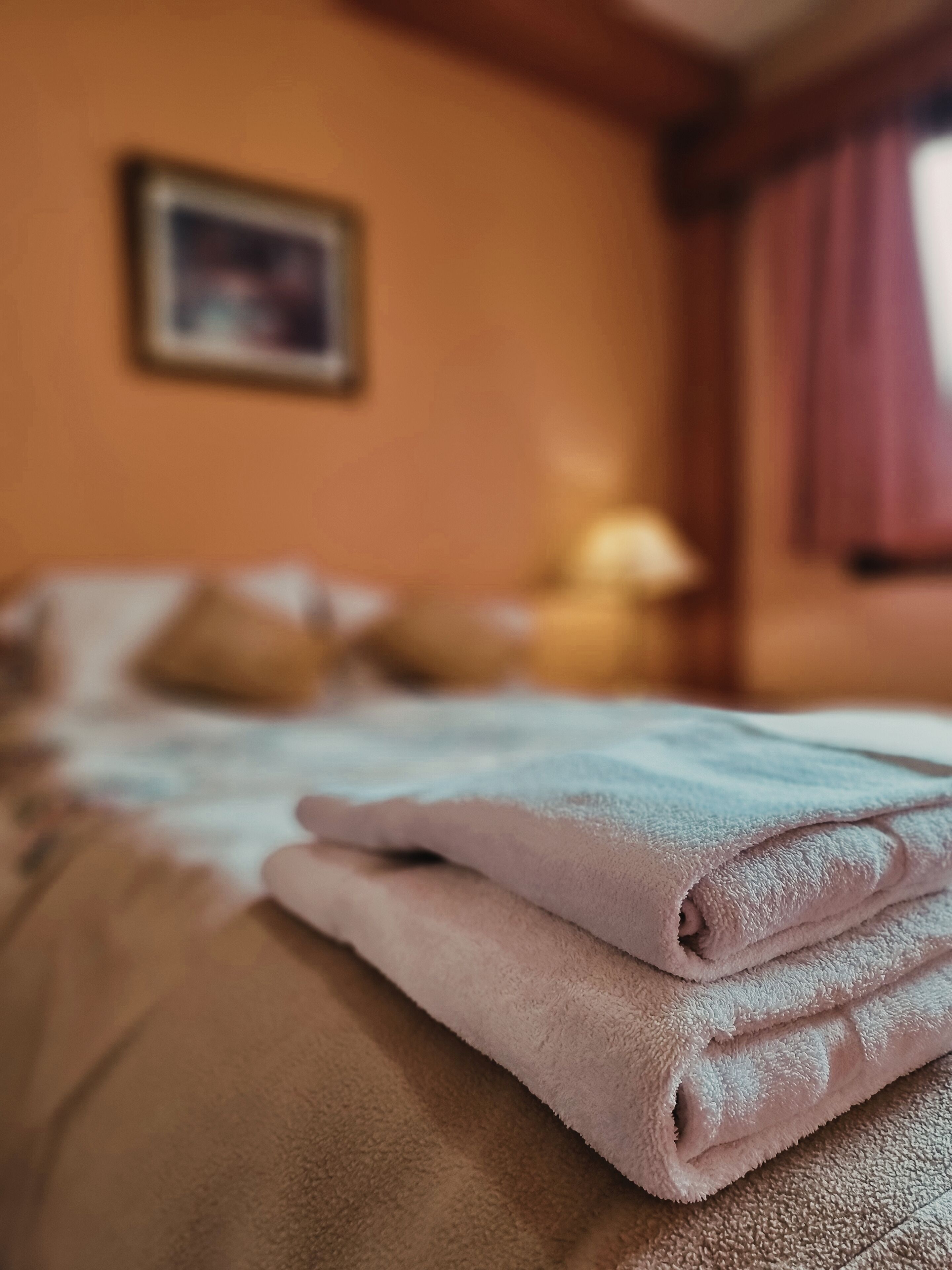 Een opgemaakt bed met gevouwen handdoeken, een ingelijst kunstwerk aan de muur en een raam met gordijnen.