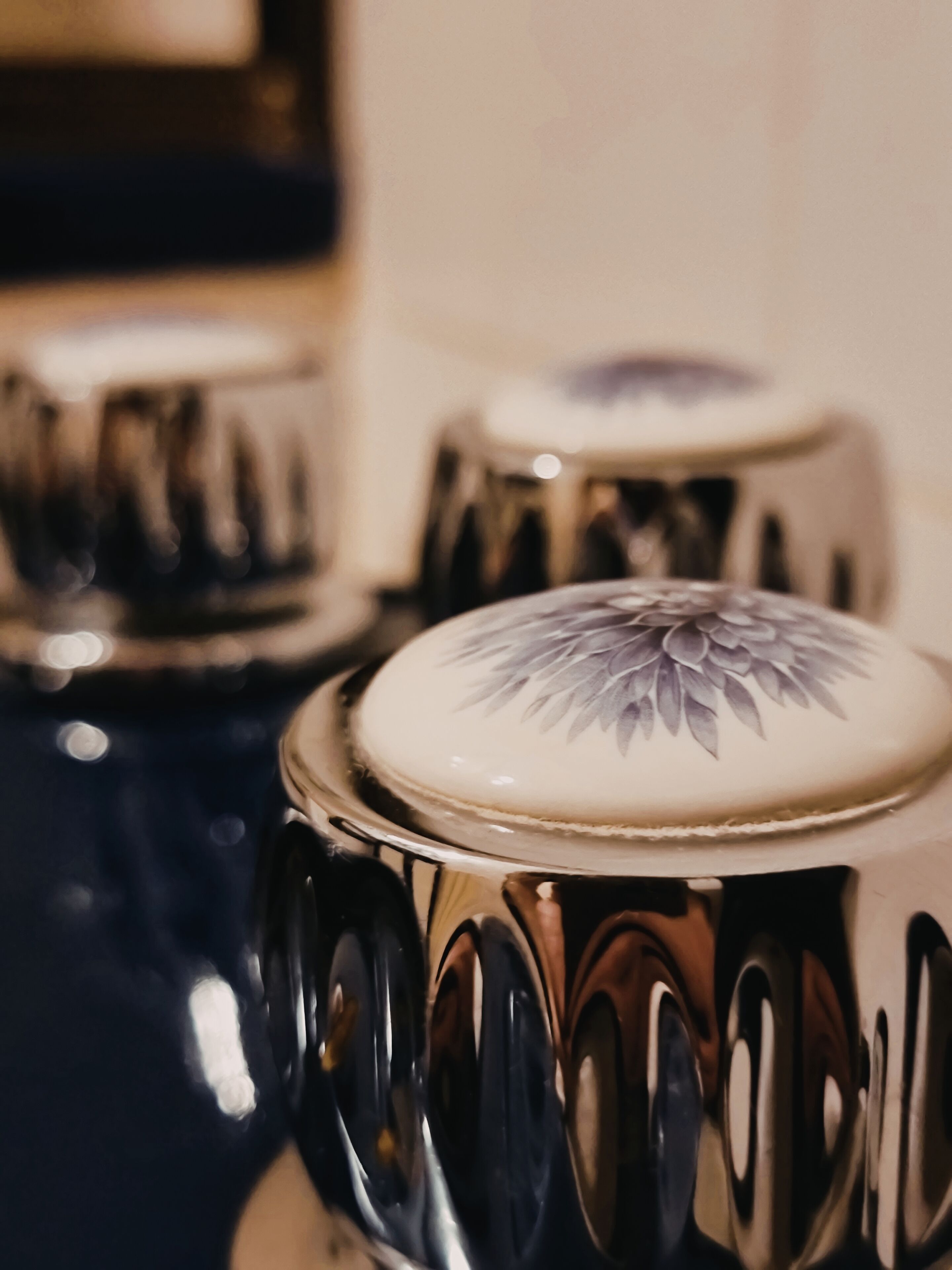 A close-up of a decorative ceramic container with a floral design on the lid, reflecting its surroundings.