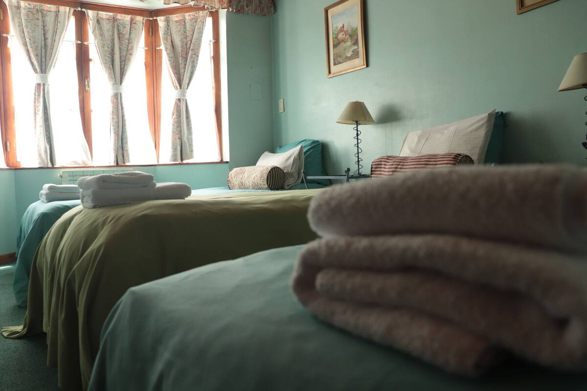 A hotel room with two beds, a window with curtains, a lamp, and a painting on the wall.