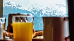 Une table avec un verre de jus d’orange et une tasse, avec une vue sur les montagnes en arrière-plan.