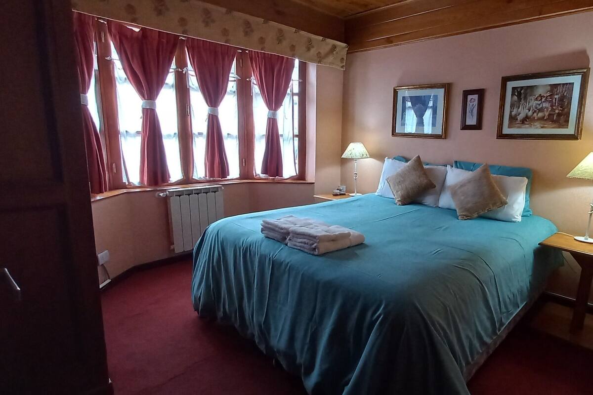 A bedroom with a bed, two bedside tables, a window with curtains, and wall-mounted pictures.