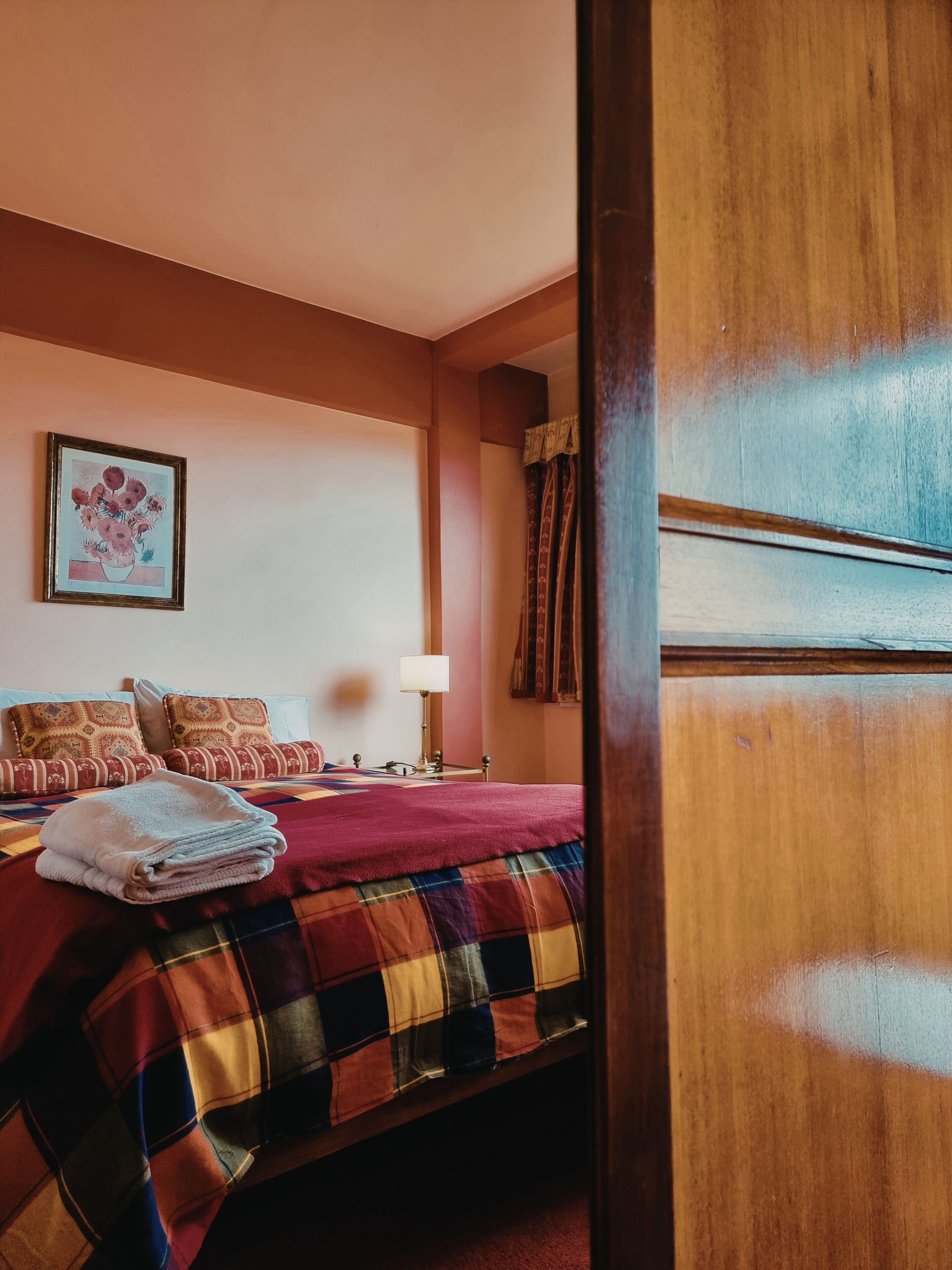 Une chambre d’hôtel avec un lit, une table de chevet, une lampe, un tableau encadré au mur et une fenêtre avec des rideaux.