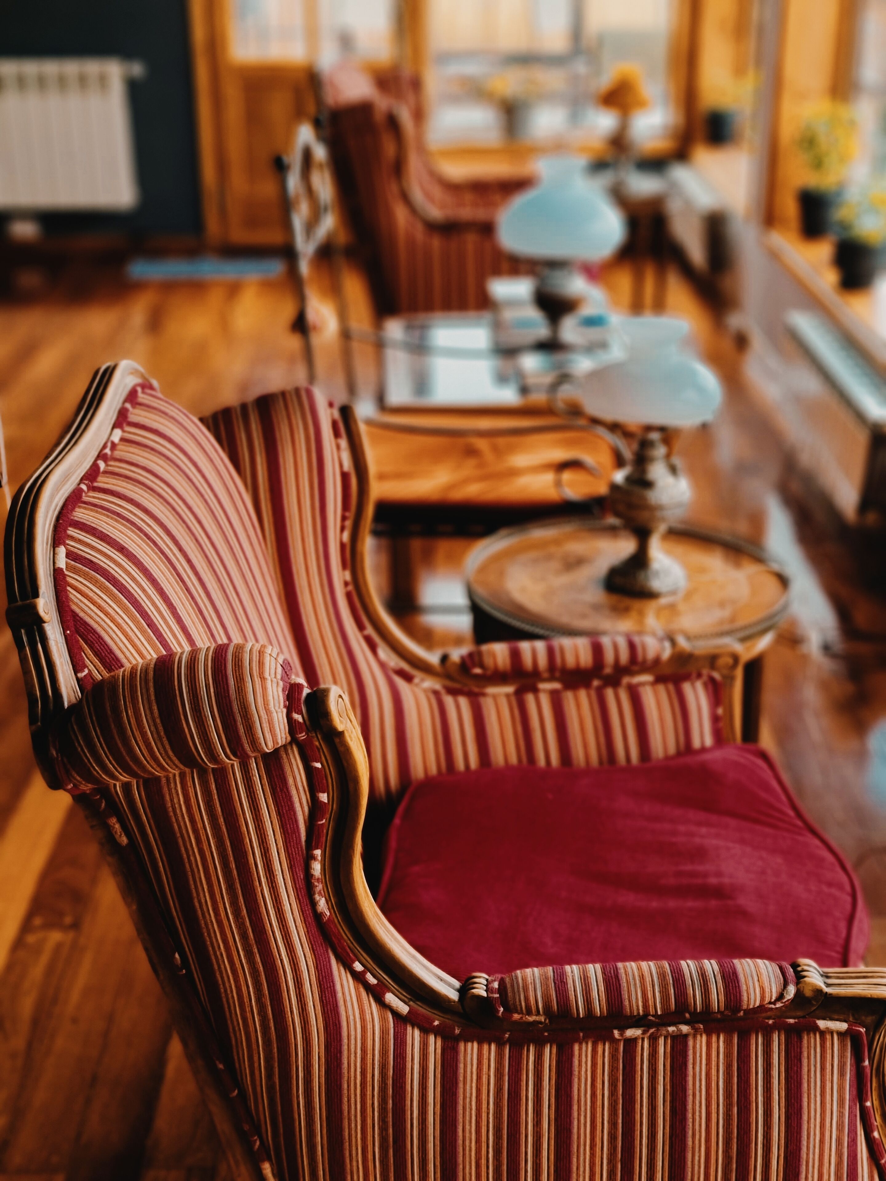 Un fauteuil à rayures avec un coussin rouge, dans une pièce chaleureuse éclairée d’une lumière douce, dotée d’un plancher en bois et de meubles en bois.
