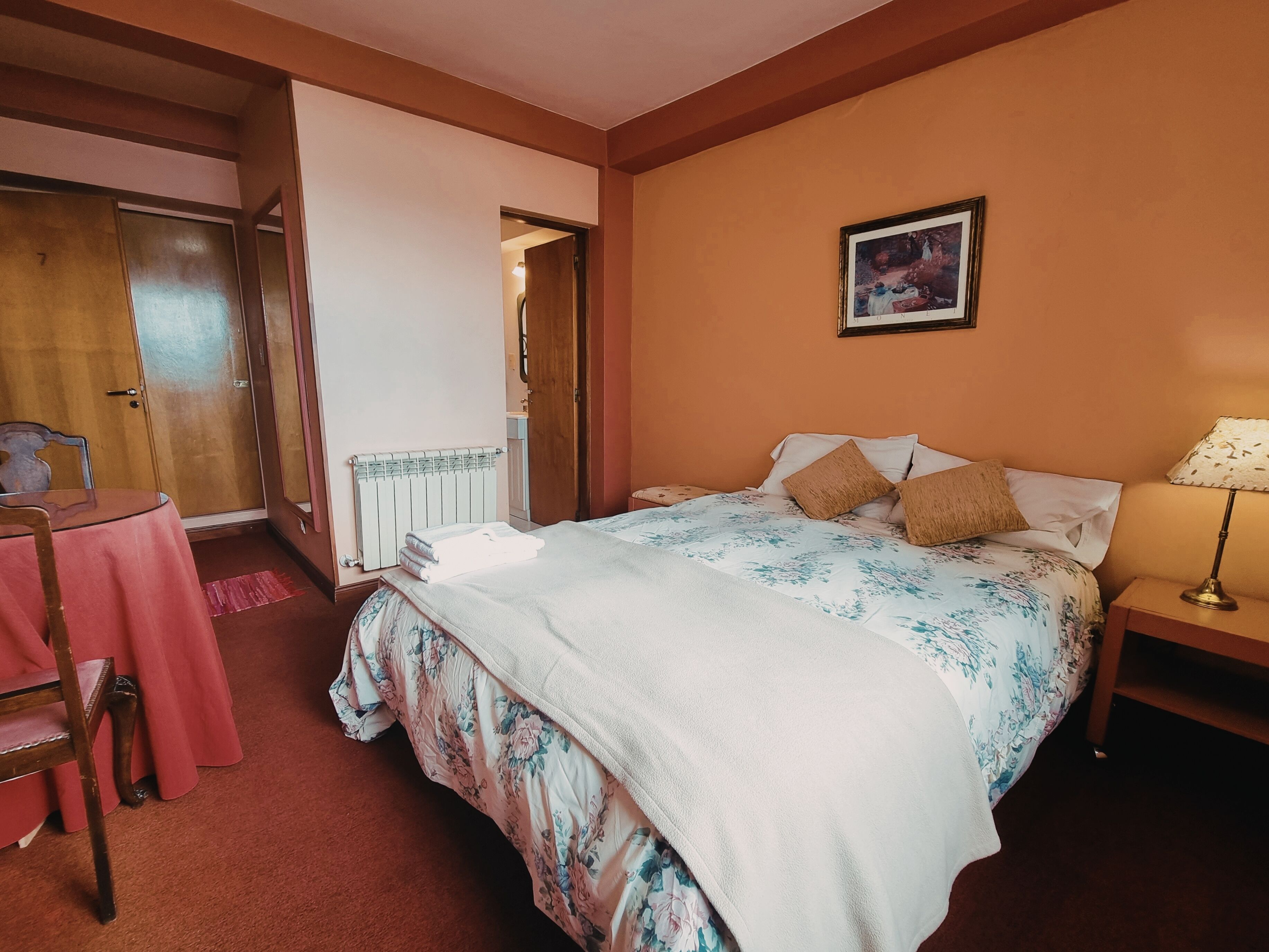 Une chambre à coucher avec un lit, une table de chevet, une lampe, une chaise et une table recouverte d’une nappe rose.