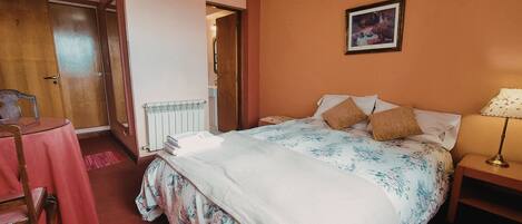 Un dormitorio con cama, mesita de noche, lámpara, silla y mesa con mantel rosa.