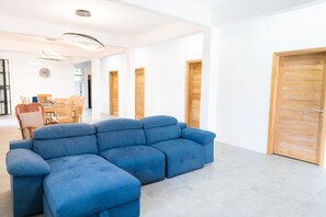 A modern living room with a blue sectional sofa, wooden doors, and a dining area with chairs and a table. - Spacious Villa with swimming pool steps away from the beach (Pamplemousses District)