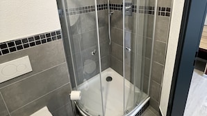 A corner shower with a glass enclosure, a toilet, and tiled walls. - Yebs Hotel (Guenzburg)
