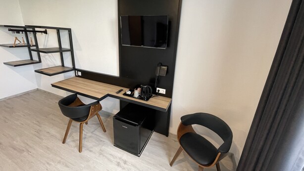 A modern office space with a long desk, two black chairs, a black filing cabinet, and a mounted flat-screen TV. - Yebs Hotel (Guenzburg)